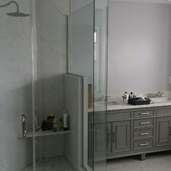 Bathroom with glass shower, white walls, and a gray vanity with a sink and toiletries.