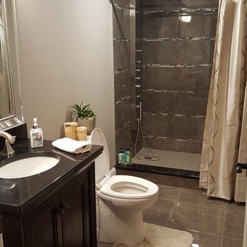 Modern bathroom with dark tile, vanity, toilet, and glass shower stall