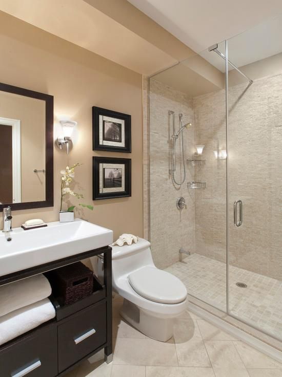 Modern beige bathroom with glass shower, white vanity, and toilet near tiled walls.