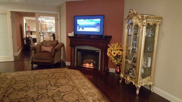 Cozy living room with lit fireplace, TV, armchair, ornate cabinet, and patterned rug in warm tones