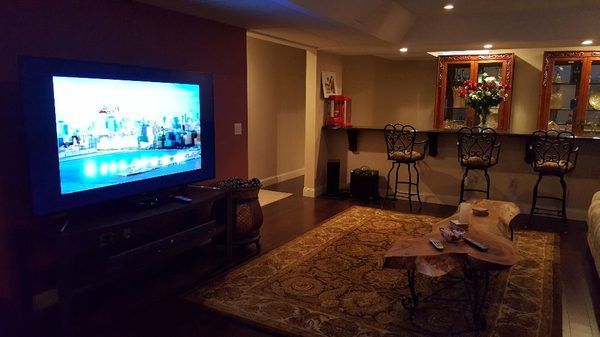 Cozy living room with a glowing TV, patterned rug, coffee table, and a bar counter in the background