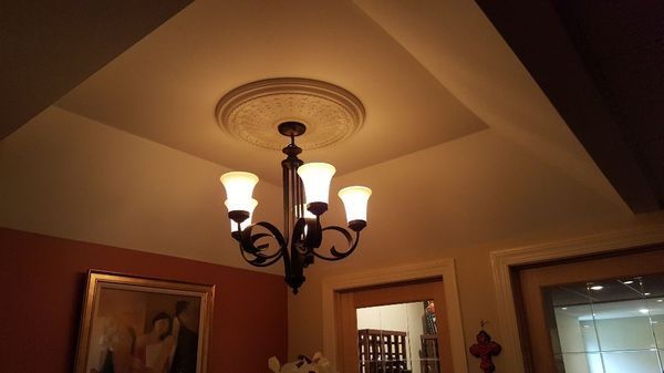 Ceiling chandelier lit in a warmly painted room with crown molding and framed wall art