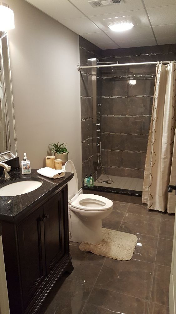 Bathroom with dark tile shower, toilet, and vanity sink, seen from the doorway.