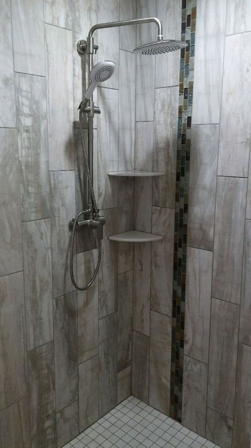 Accessible shower with grab bars, handheld showerhead, and built-in corner shelves in a tiled bathroom.