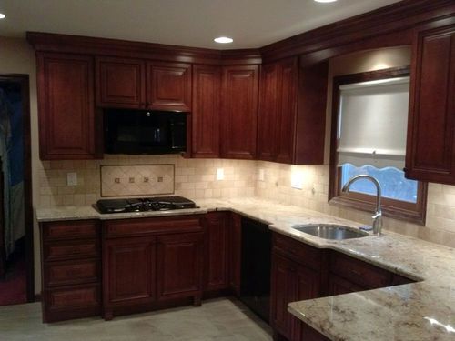 Modern kitchen with dark wood cabinets, granite counters, tiled backsplash, and a black stove under recessed lighting