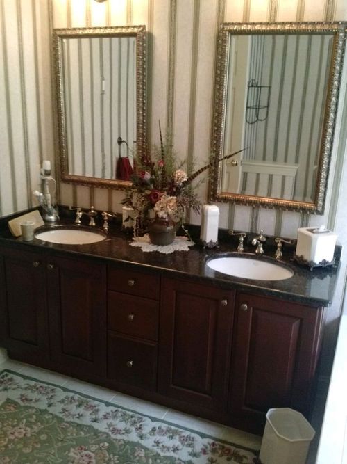 Double vanity bathroom with dark wood cabinets, granite countertop, two mirrors, and floral decor.