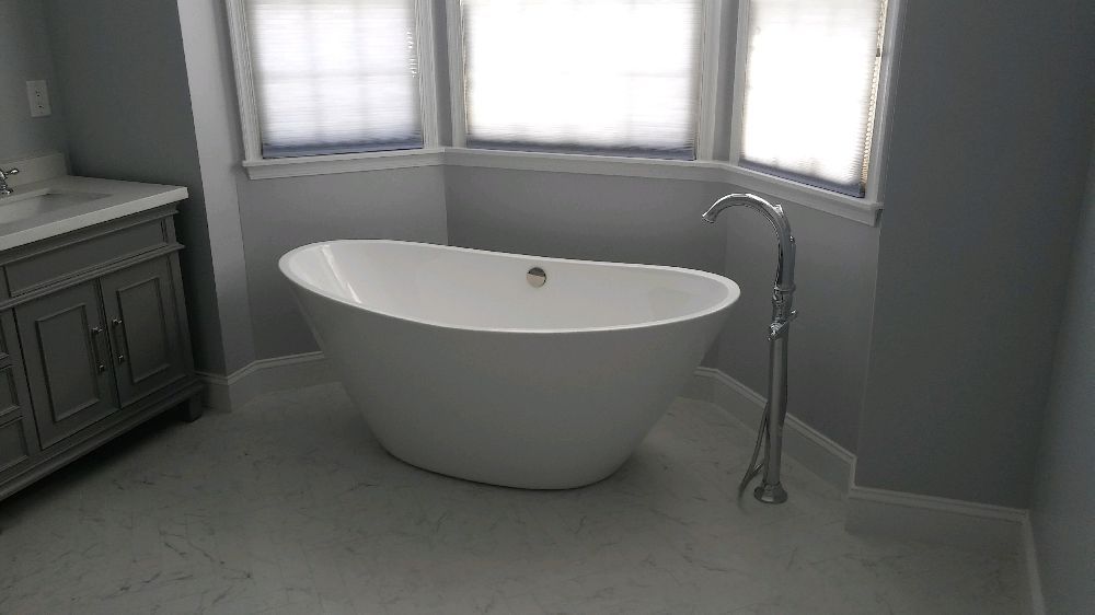 Modern bathroom with a white freestanding bathtub beneath corner windows and a chrome floor-mounted faucet