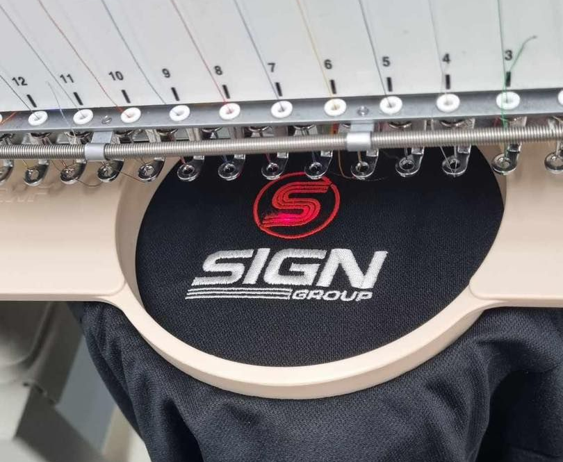 An embroidery machine stitching a red circular S logo and the white text 