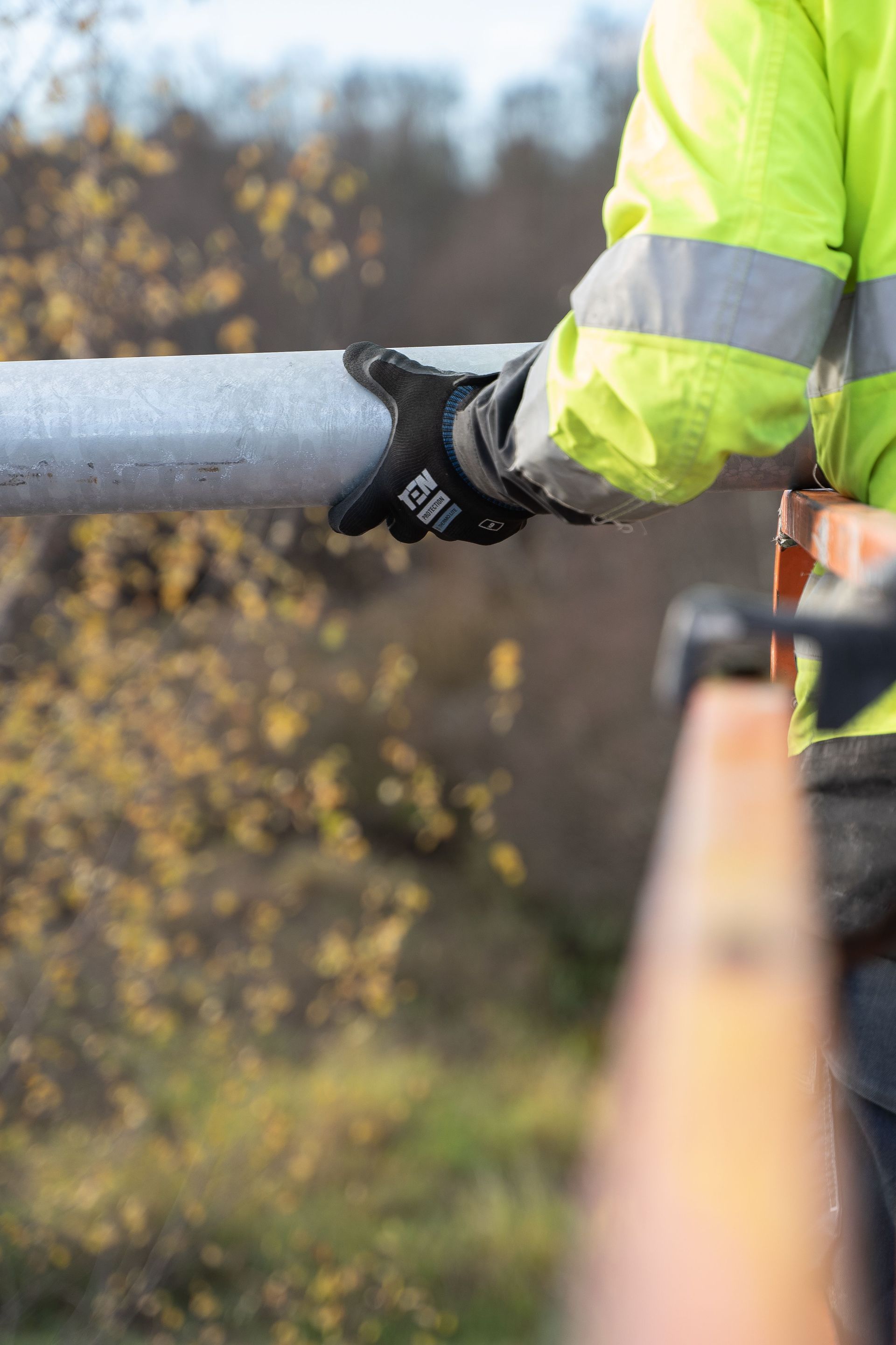 A man holding a pipe with gloves and a high vis on