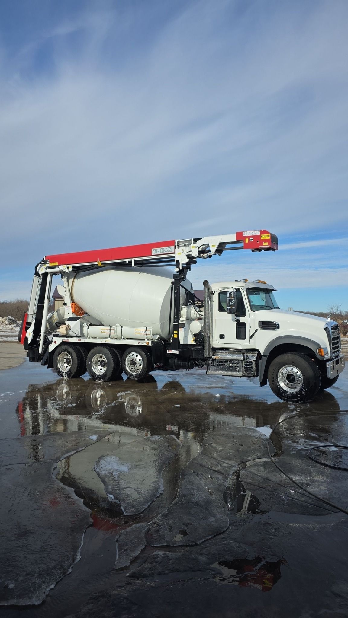 White tow truck with red crane parked on wet pavement under a cloudy sky.