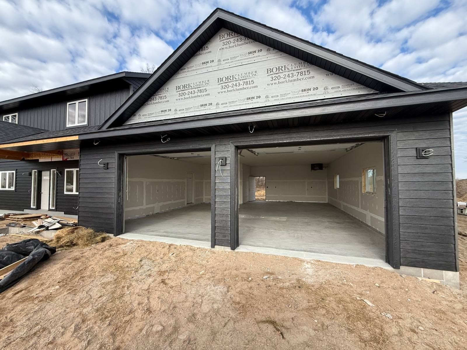 Two-car gray garage with open bays and unfinished concrete floor at a construction site