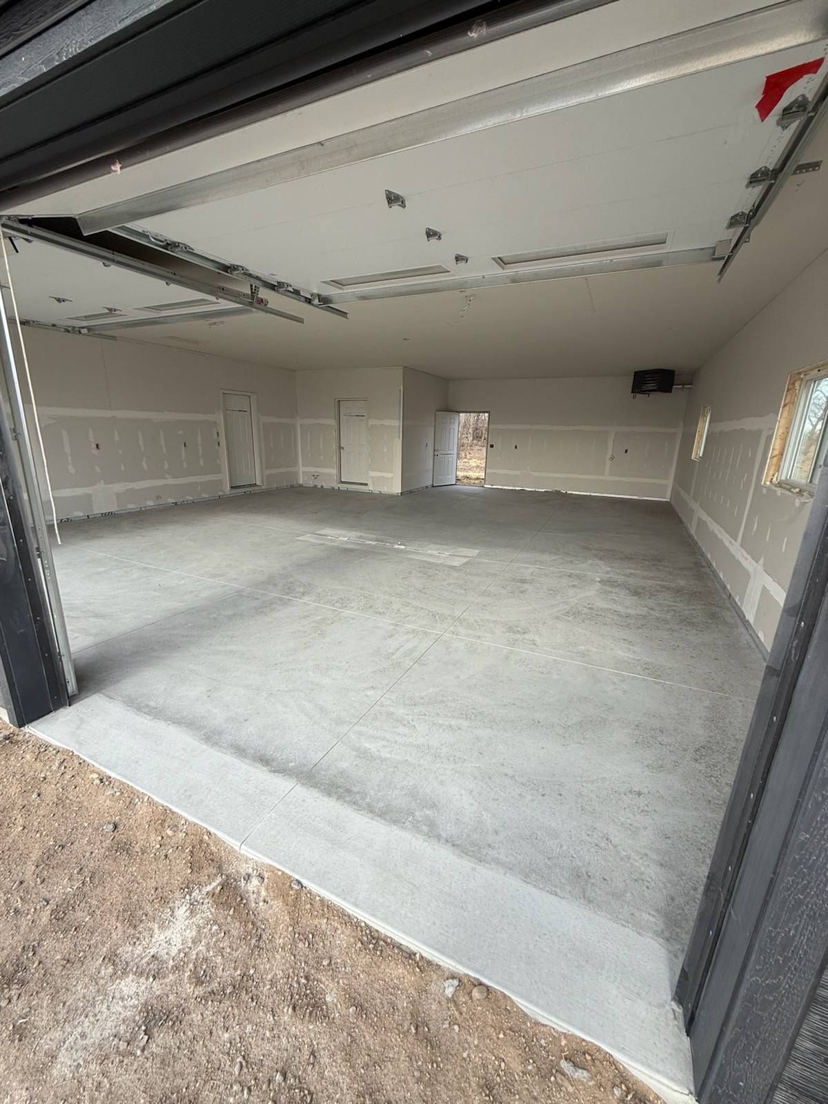Empty unfinished garage with gray concrete floor and beige drywall walls, viewed from the open doorway