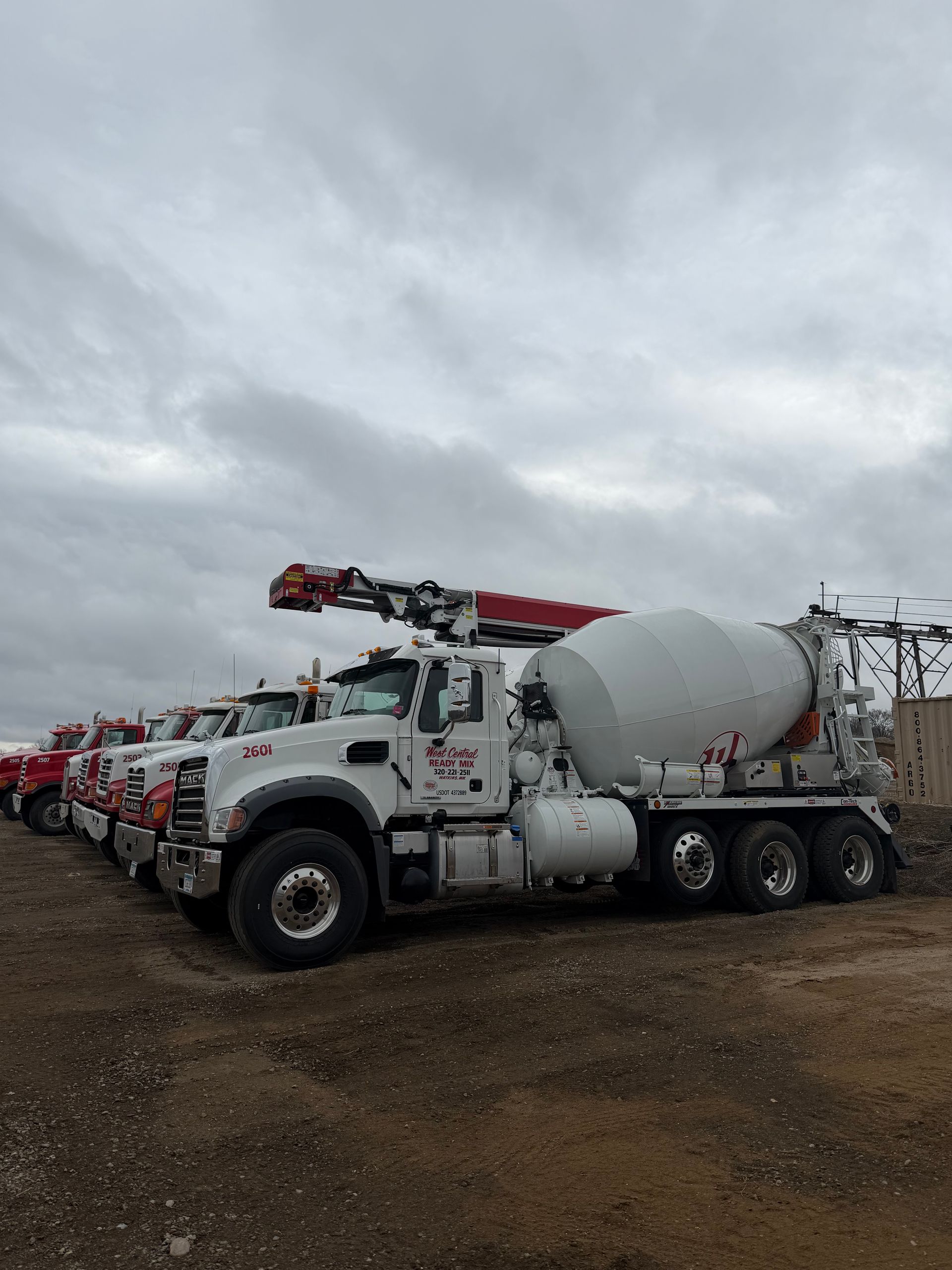 White cement mixer truck with red equipment parked on a gravel lot under a cloudy sky
