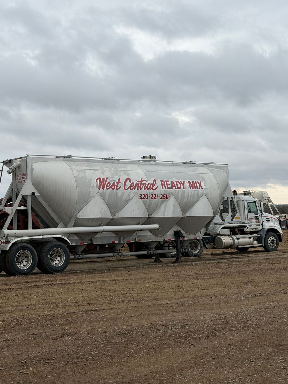 Construction workers in helmets pour concrete beside a cement mixer truck on a muddy site