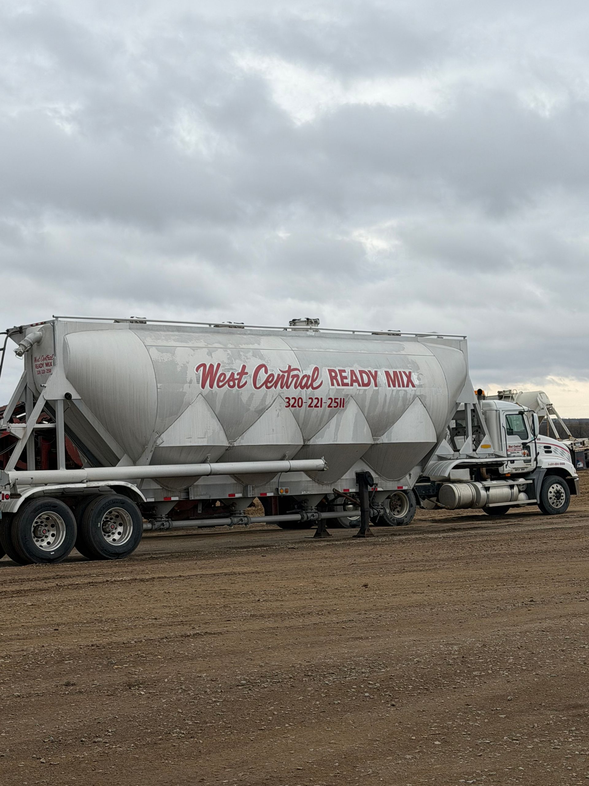 Construction workers in hard hats pour wet concrete beside a cement mixer truck at a worksite.