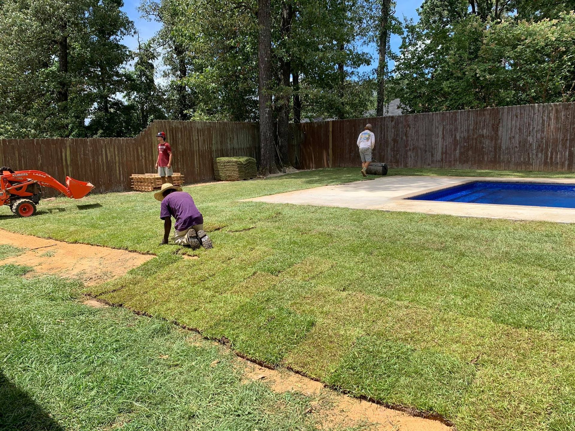 A man is working on a lawn next to a pool.