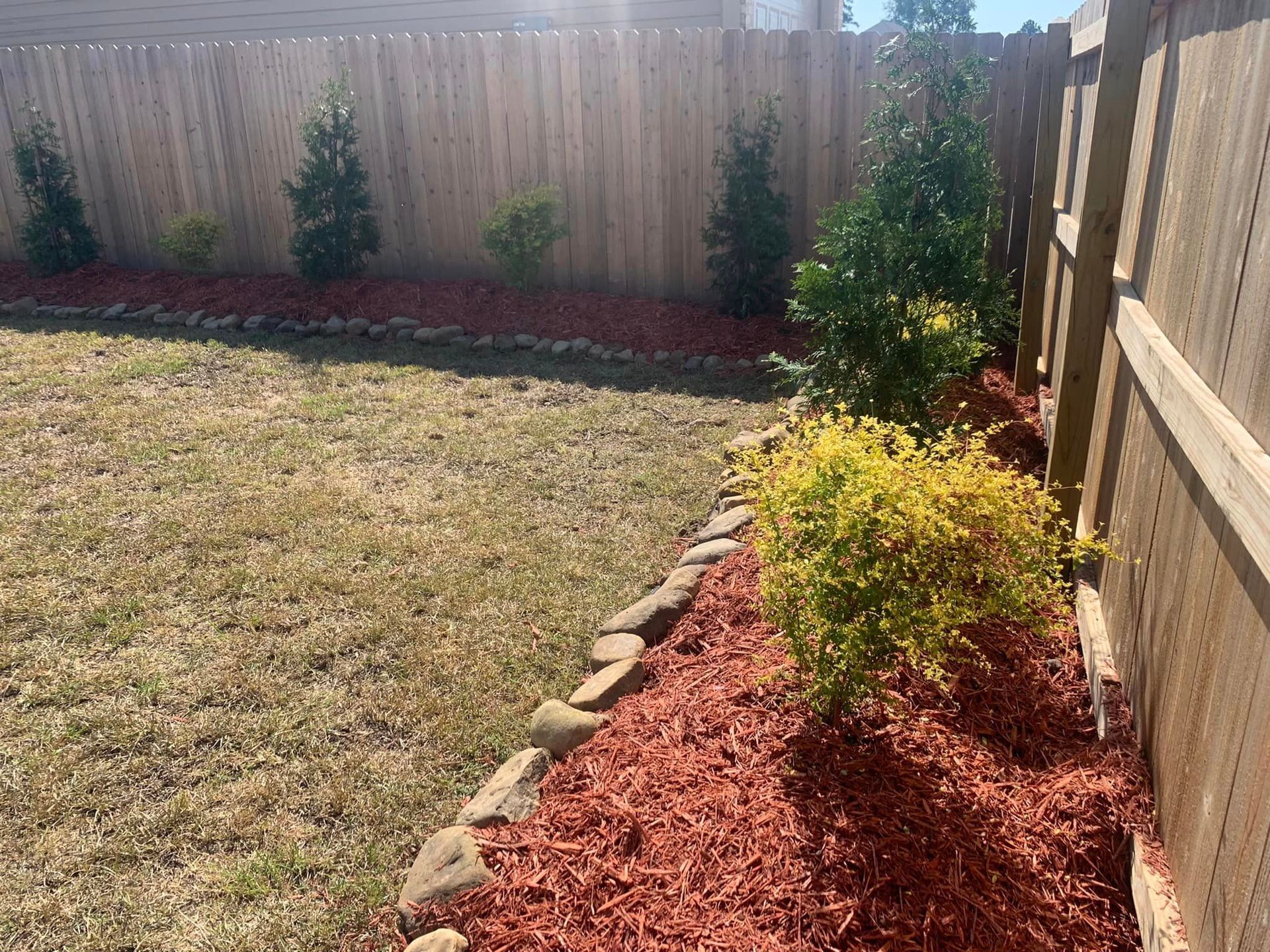 A backyard with a wooden fence and a pile of mulch.
