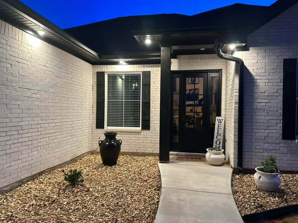 A white brick house with a black door and shutters at night.