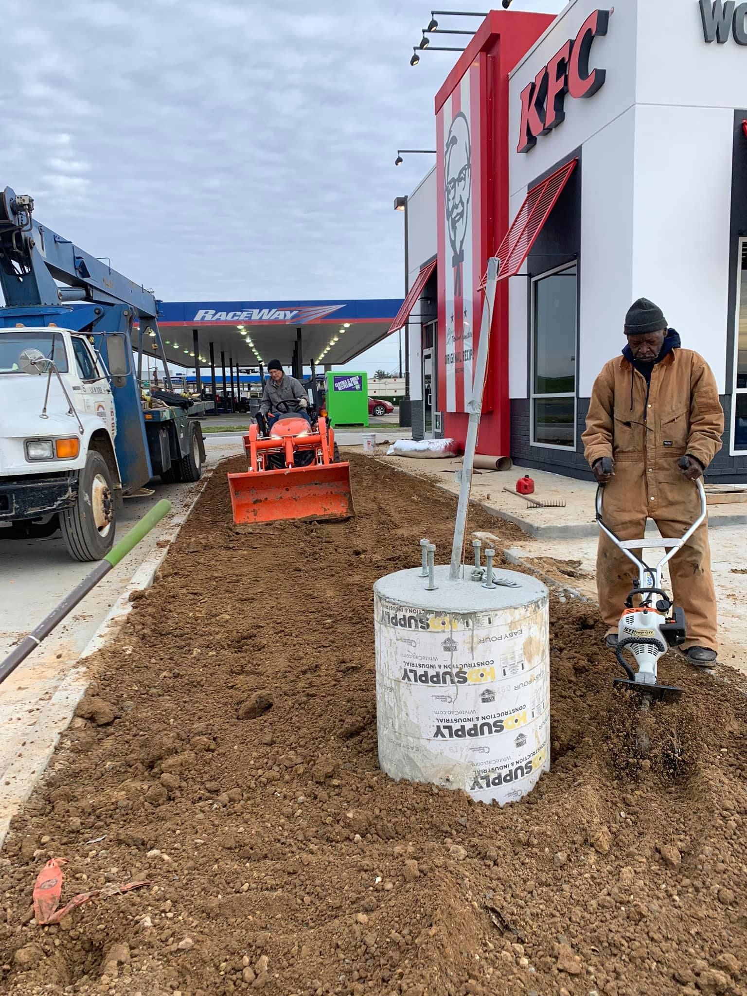 A man is digging a hole in the dirt in front of a kfc restaurant.