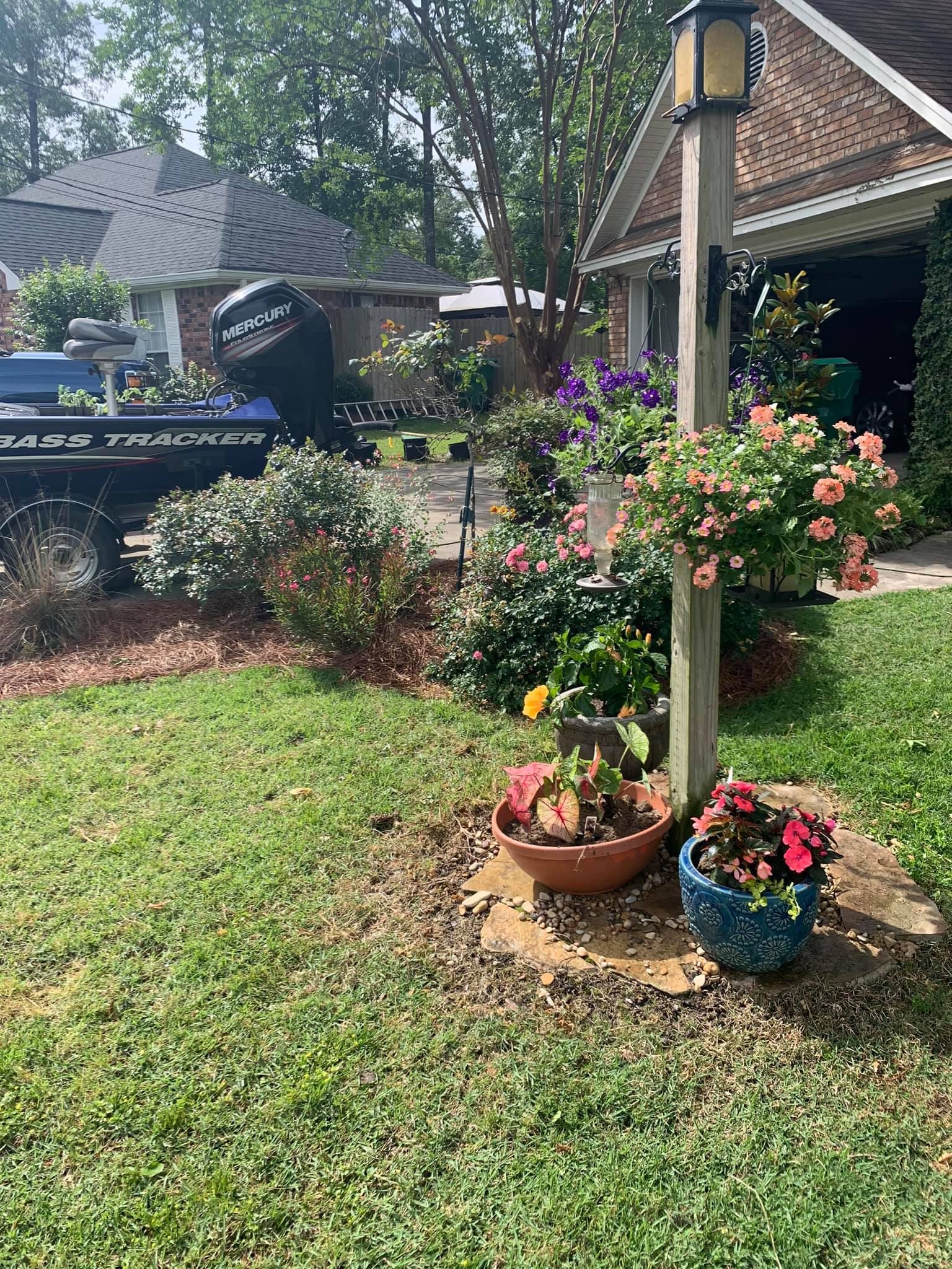A house with a boat in the backyard and flowers in front of it.