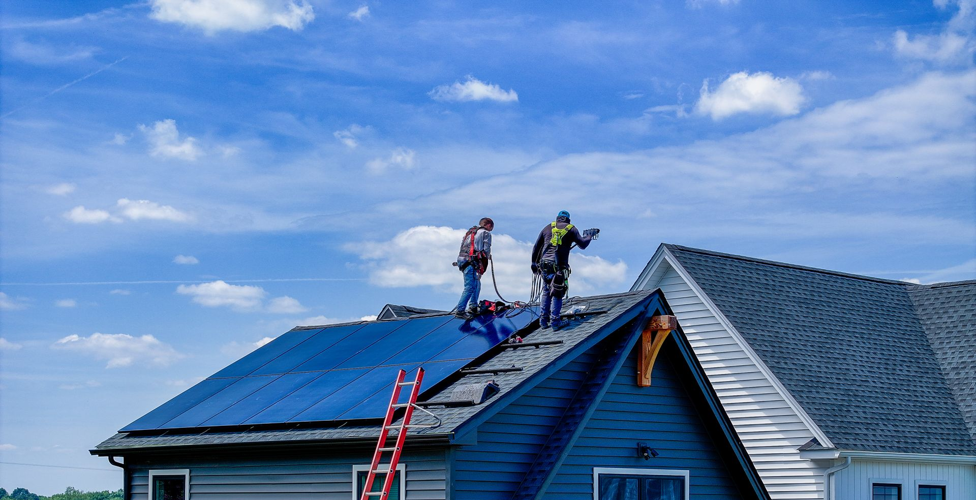 Two workers on a blue roof, installing shingles under a partly cloudy sky