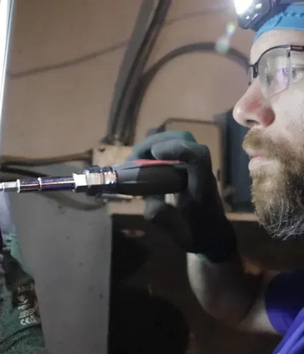 Technician in safety glasses and gloves using a power tool in a workshop