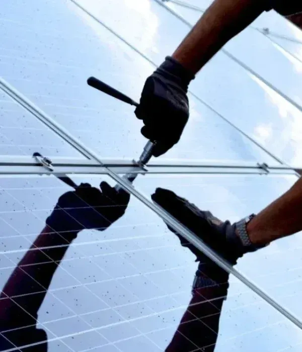 Worker using a wrench to tighten bolts on a metal structure, viewed from below against the sky.