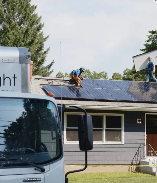 Worker installing solar panels on a rooftop beside a truck and building.