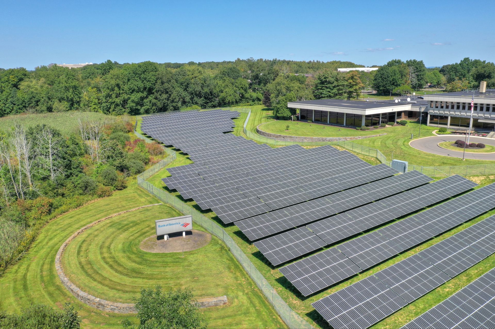 Large solar farm with rows of panels on grassy hills beside a building and trees