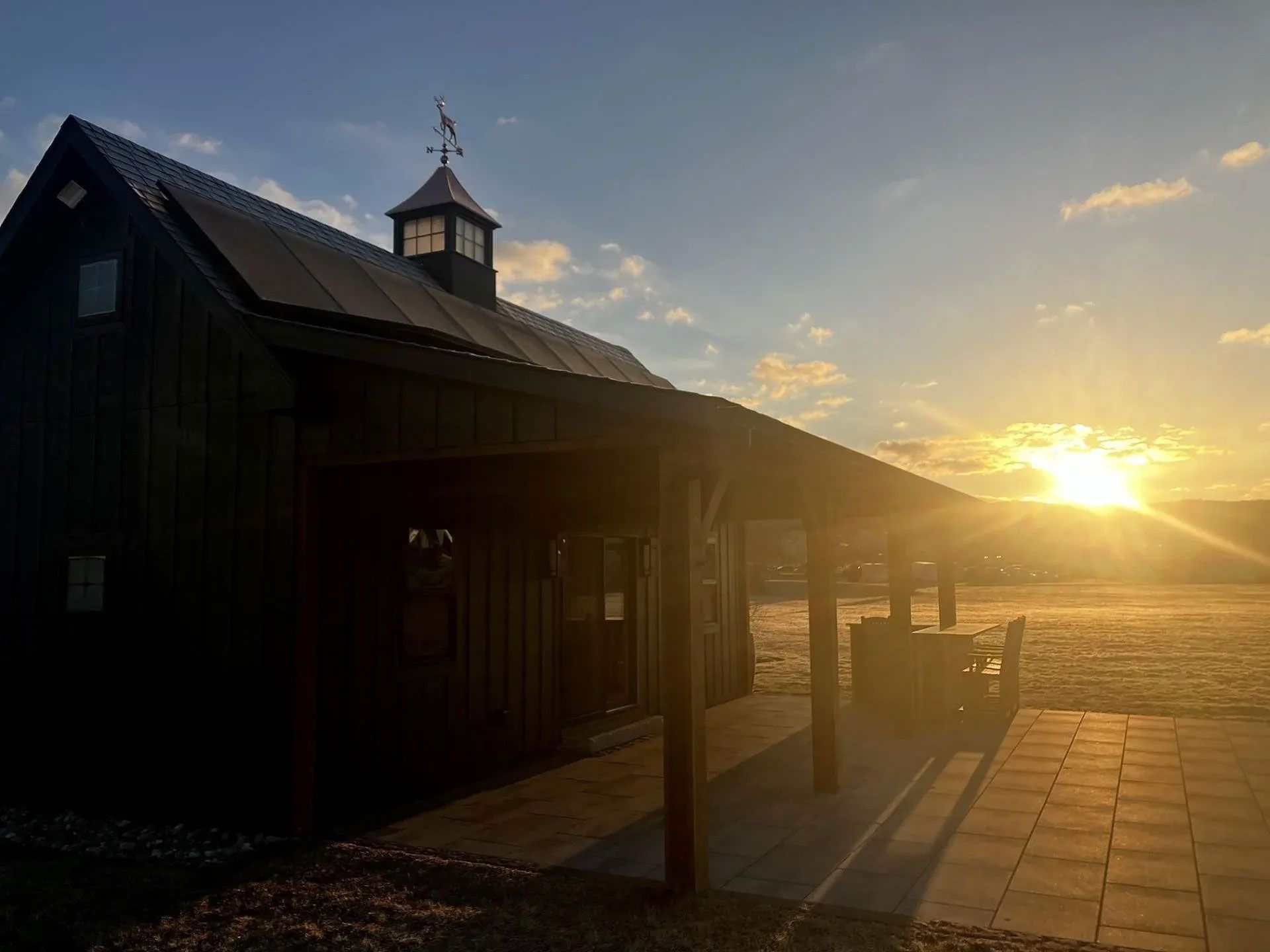 Sunset over a dark wooden seaside pavilion with a lit walkway and open beach beyond