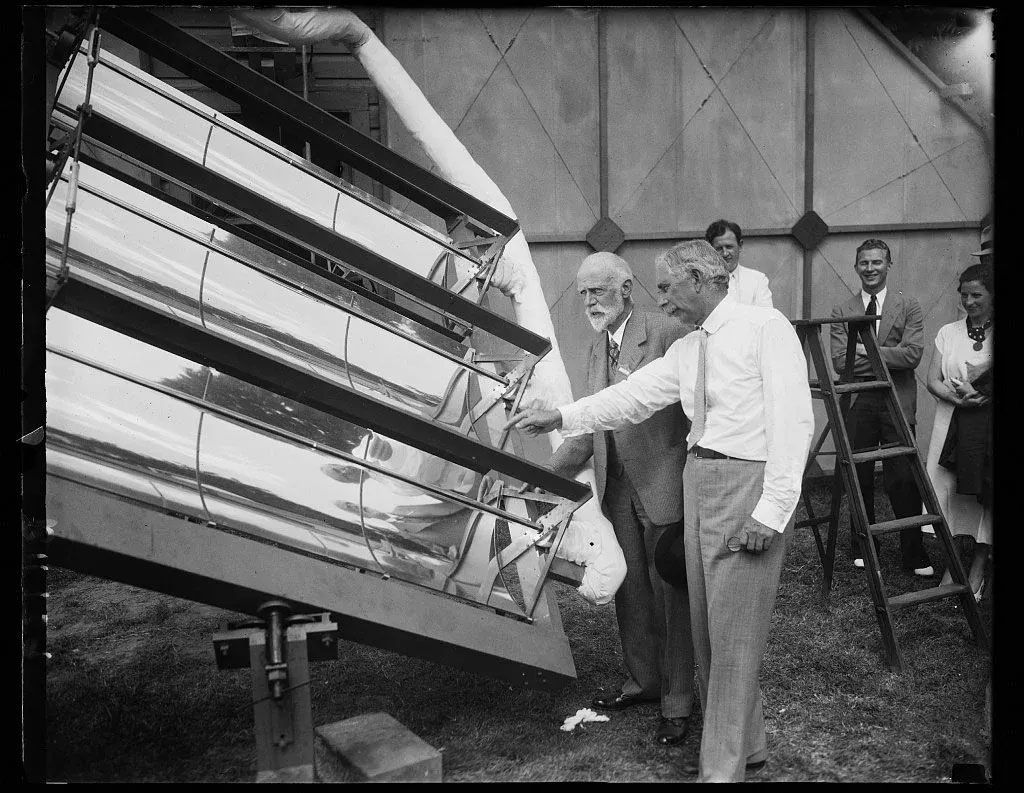 Men examining a large slanted machine with rows of lights in a tent-like pavilion.