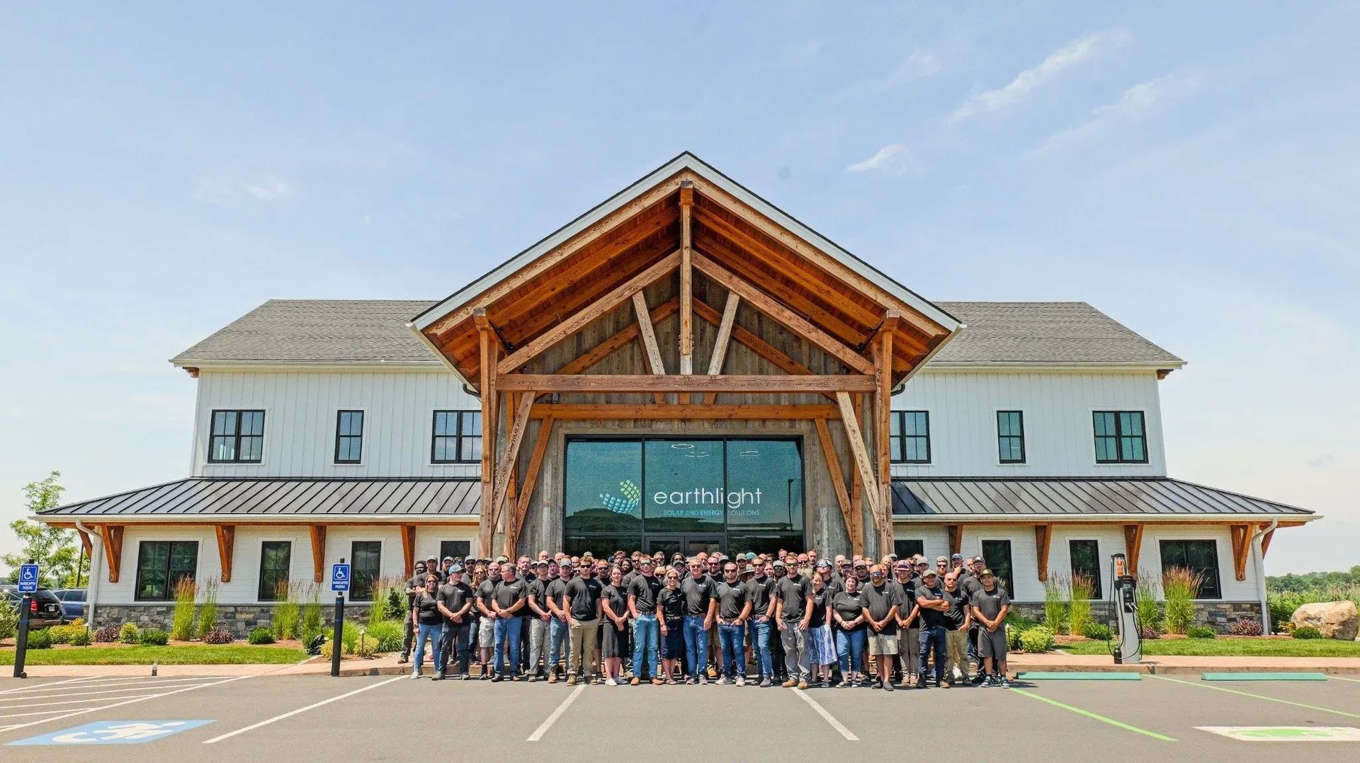 Large group posing outside a modern lodge-style building with a wooden entrance and peaked roof.