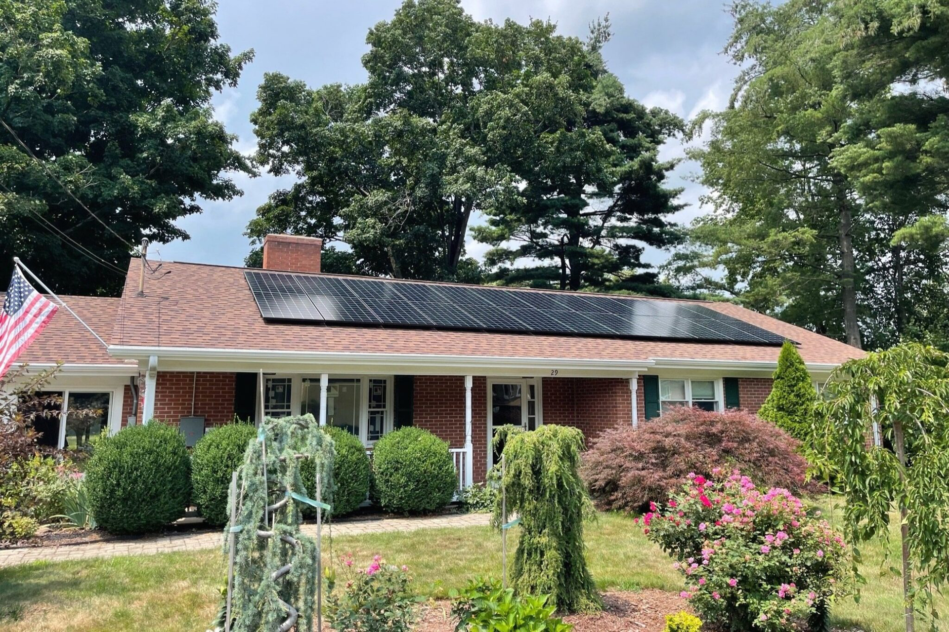 Single-story brick house with solar panels, white porch, and a landscaped front yard.