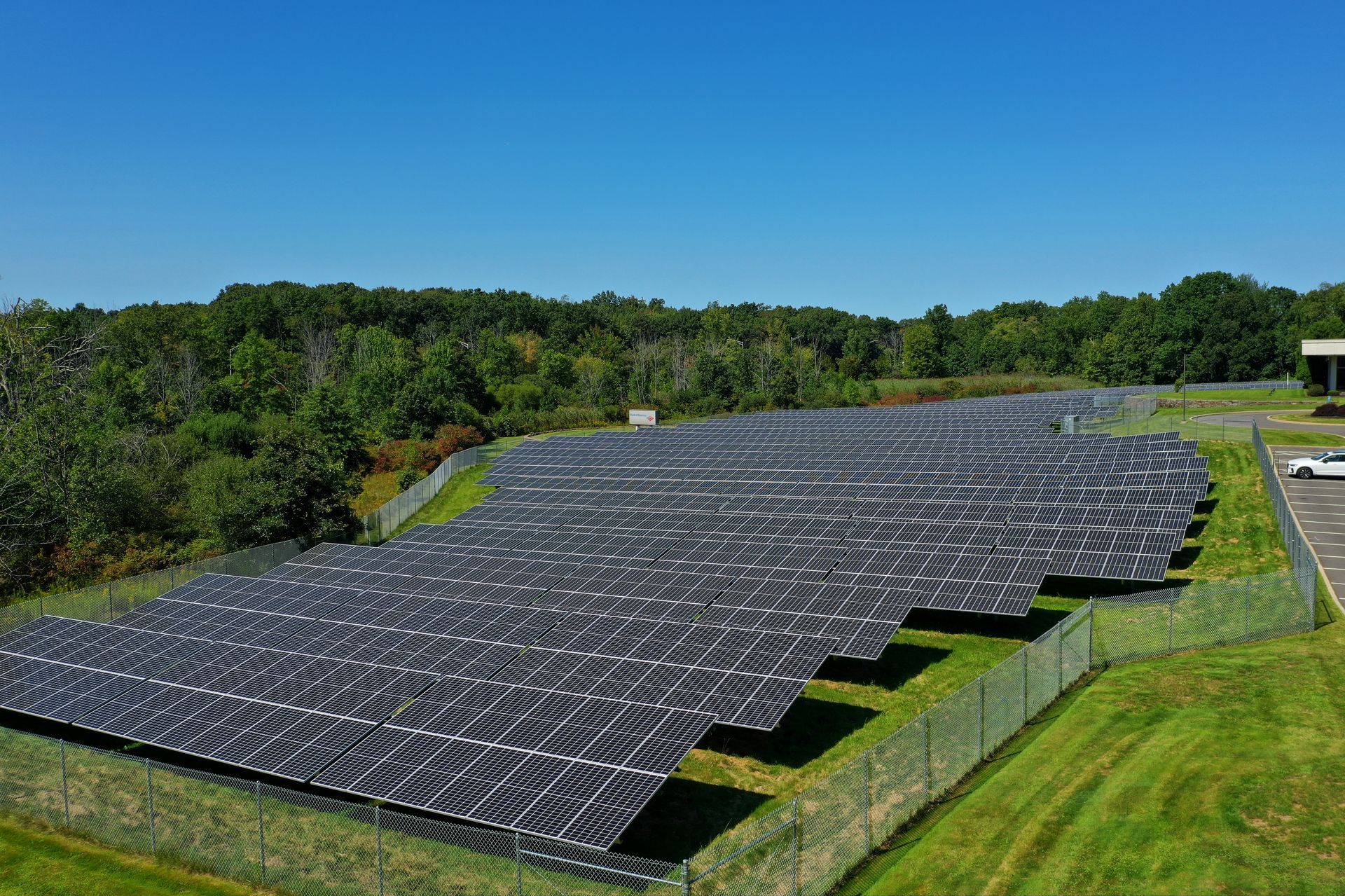 Large solar panel array on a grassy hillside with trees and blue sky in the background