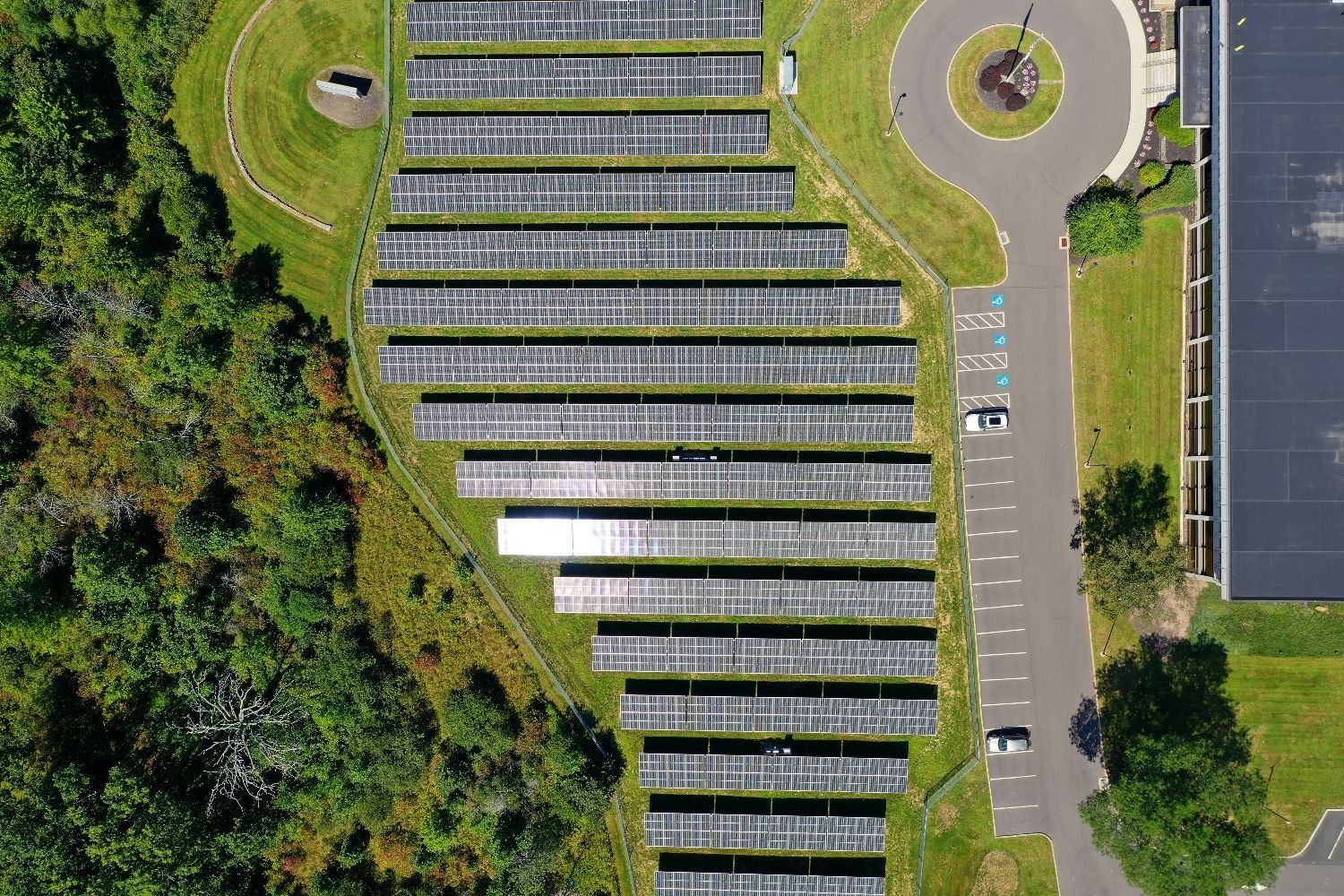 Aerial view of solar panel rows beside a road and trees in a parking lot-like area