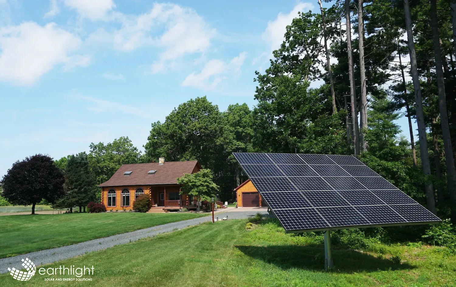 Rural house and trees beside a large solar panel array on a sunny green lawn