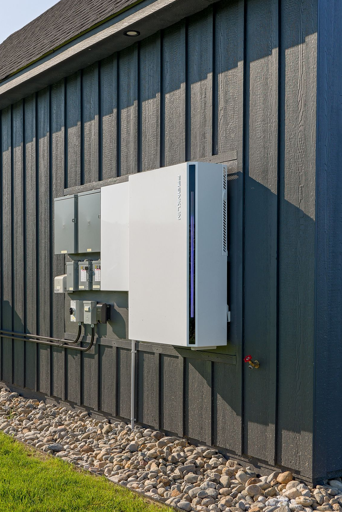 White electrical equipment mounted on a dark exterior wall beside a small fence.