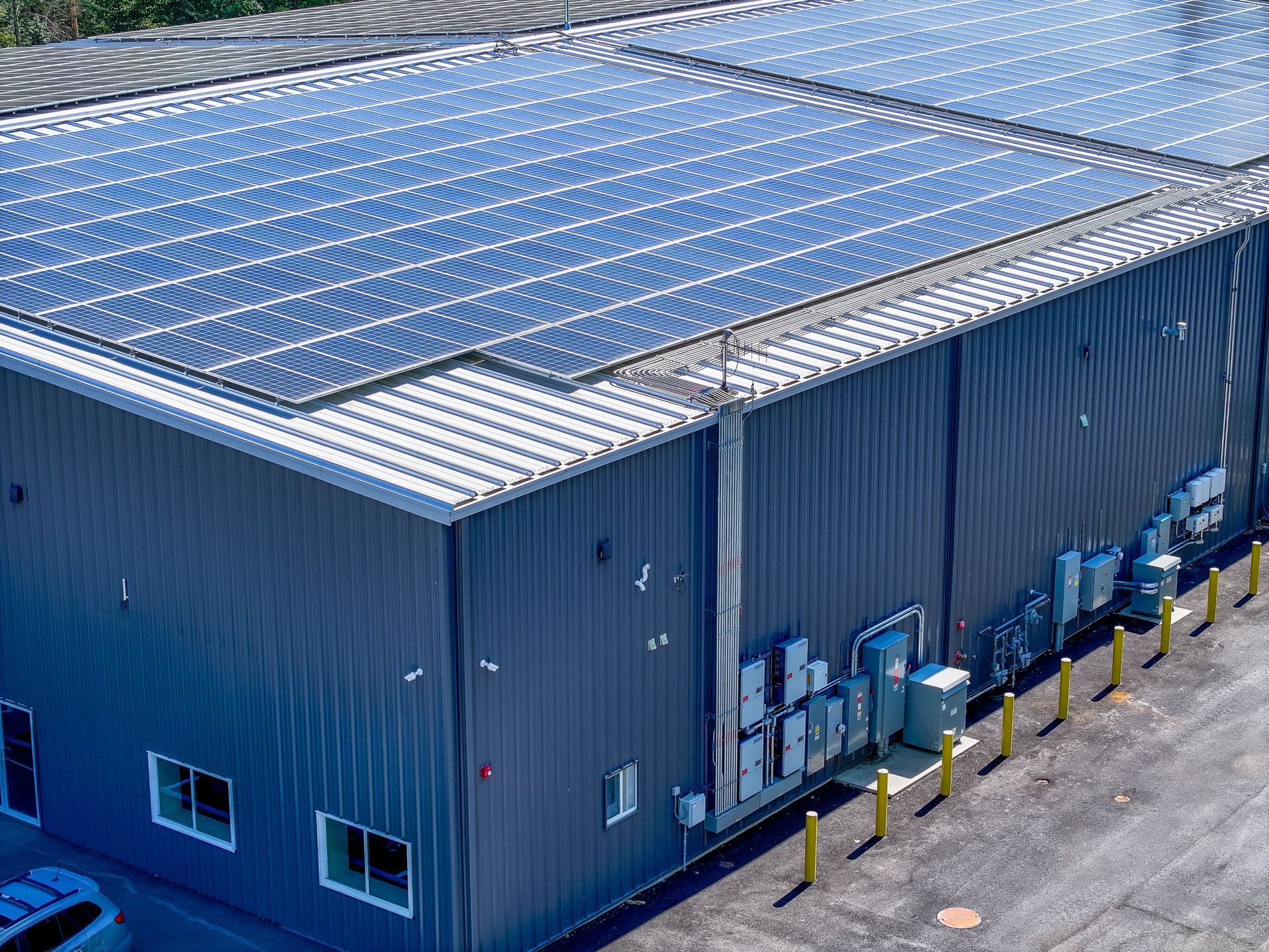 Blue industrial building with rooftop solar panels and a row of yellow bollards outside