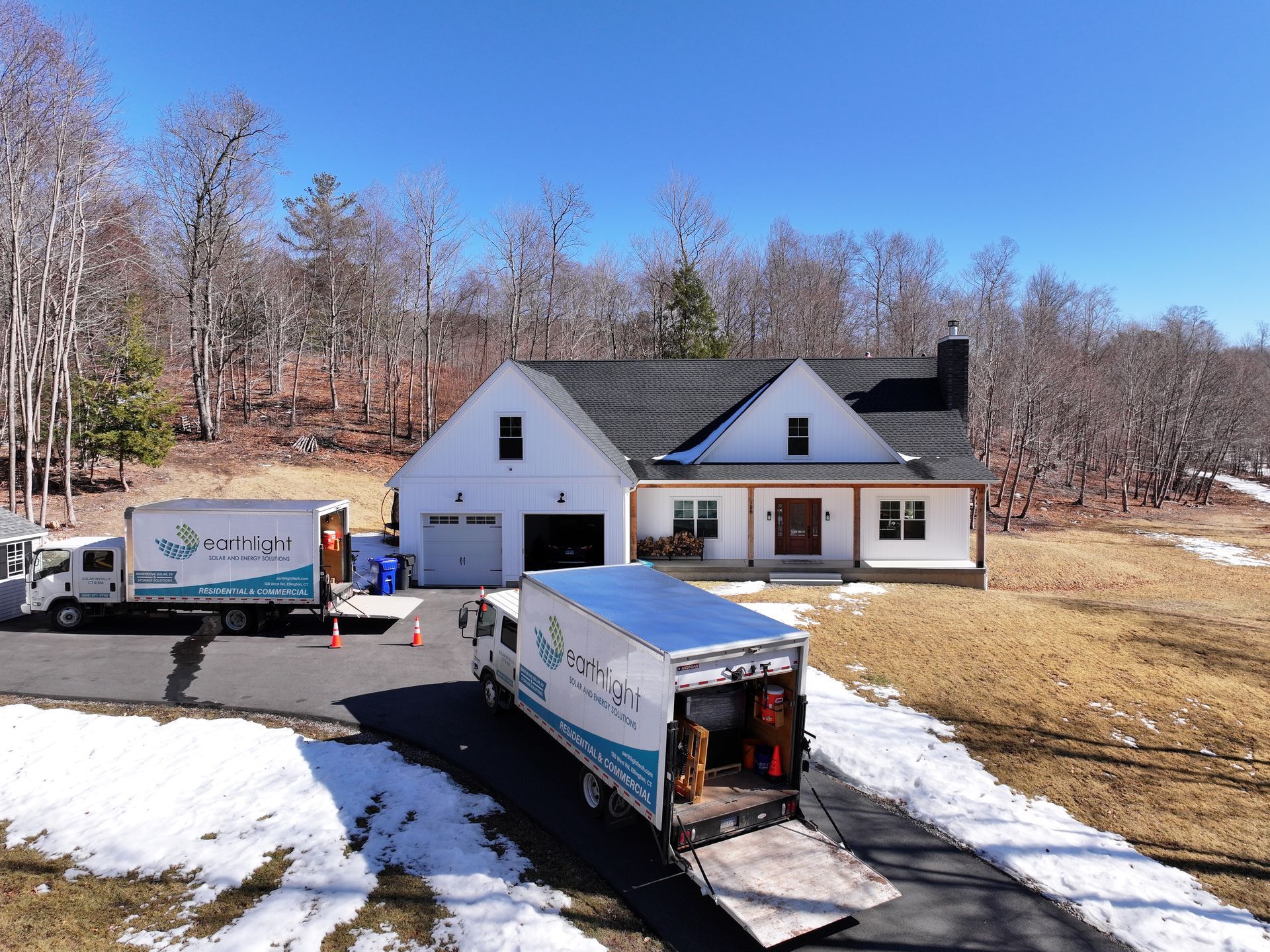 White house with moving trucks in driveway on a snowy hillside under a clear blue sky