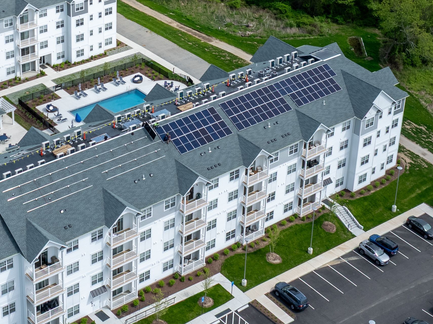 Aerial view of a white apartment complex with rooftop solar panels, pool, and parking lot