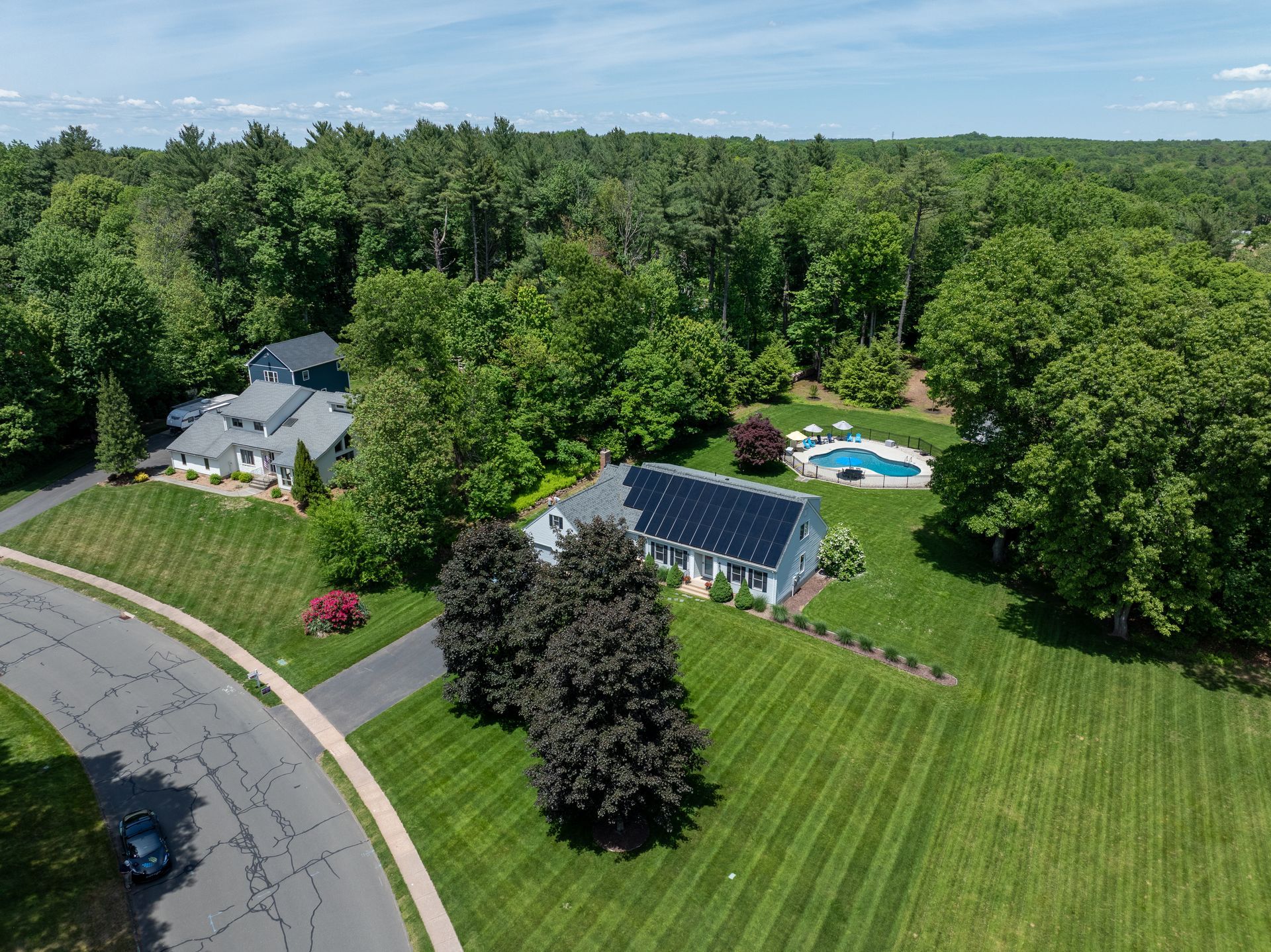 Aerial view of a house, solar-paneled building, and backyard pool surrounded by green trees and lawn