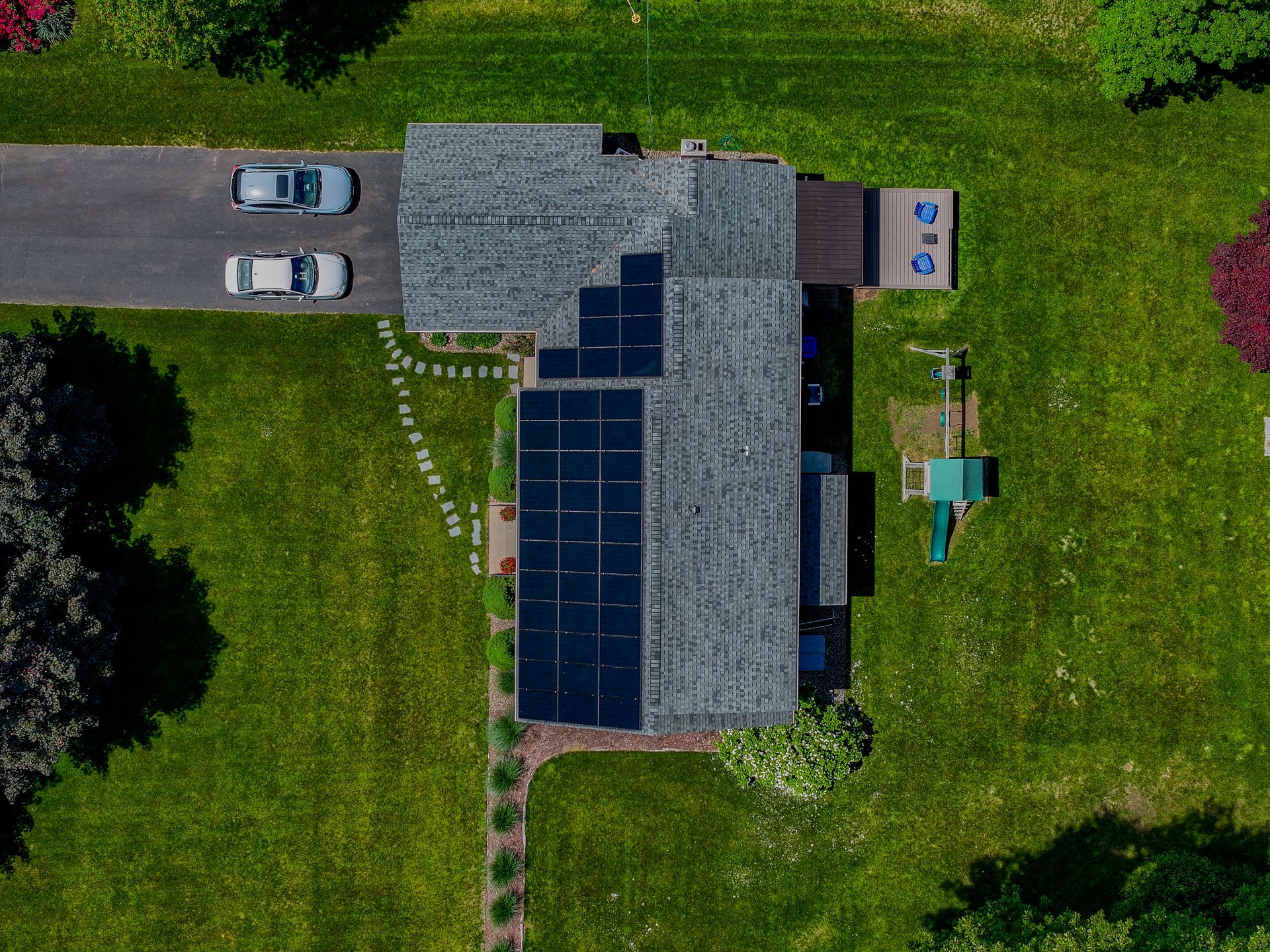 Aerial view of a house with solar panels, a driveway with two cars, and a grassy yard.