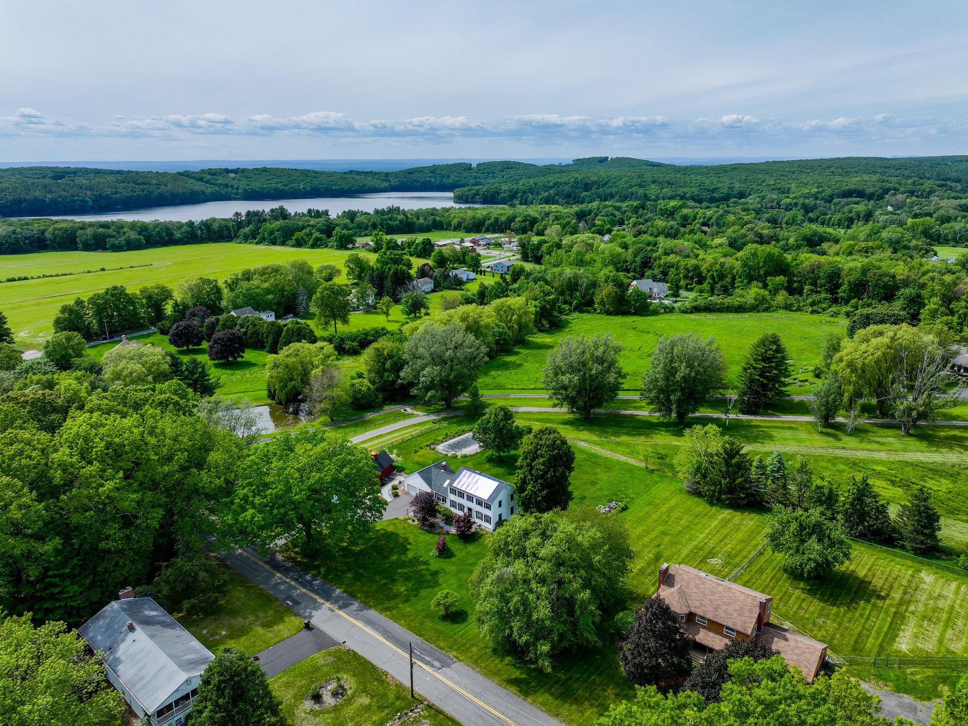 Aerial view of a green rural neighborhood with houses, roads, trees, and fields near a lake