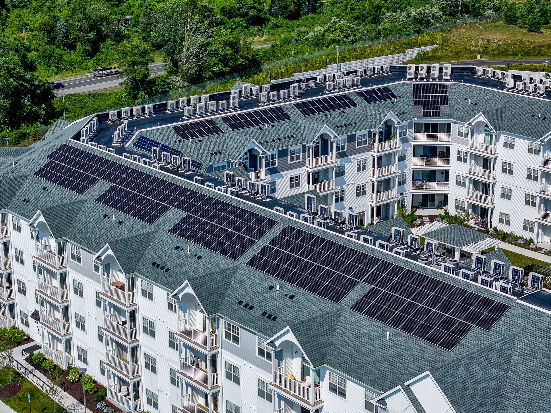 Aerial view of a white apartment complex with green roofs and rooftop solar panels surrounded by trees