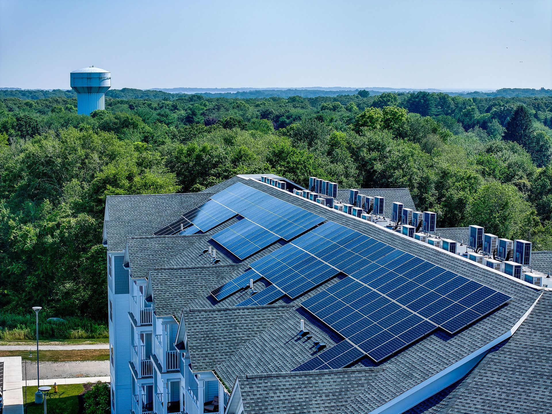 Rooftop solar panels on a building with a blue water tower and dense green trees in the background