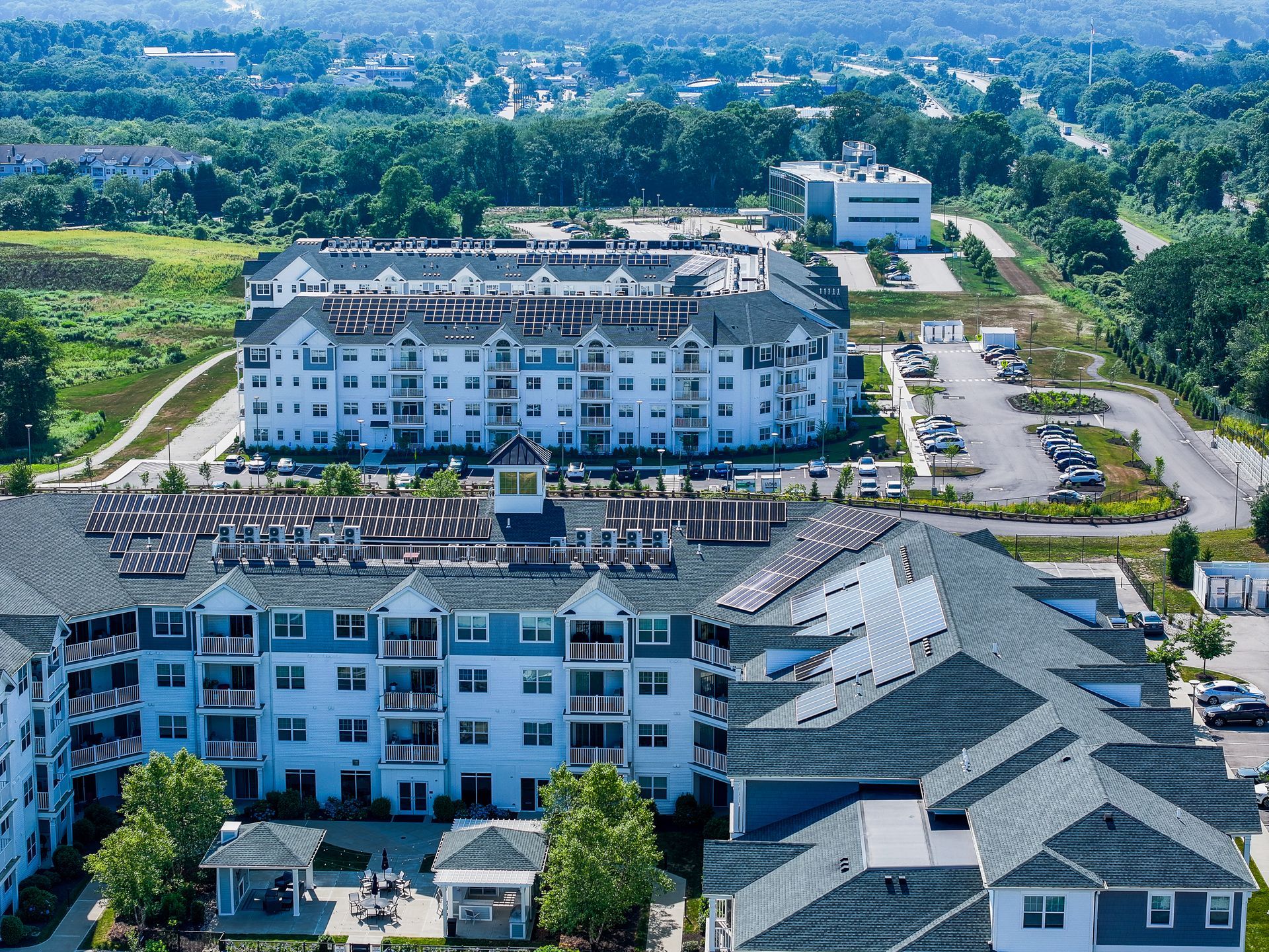 Aerial view of a white apartment complex and nearby buildings in a green suburban area
