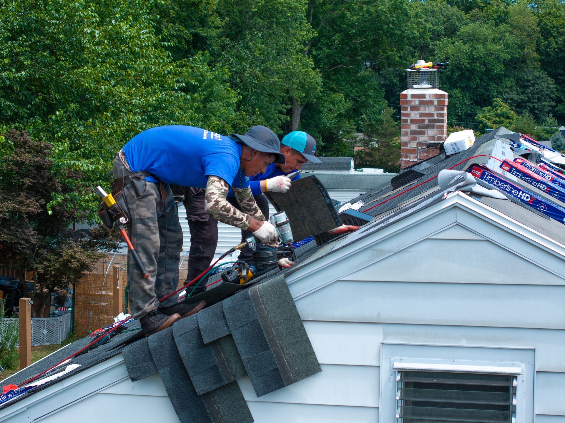 Roofers working on a house roof with tools and roofing materials.