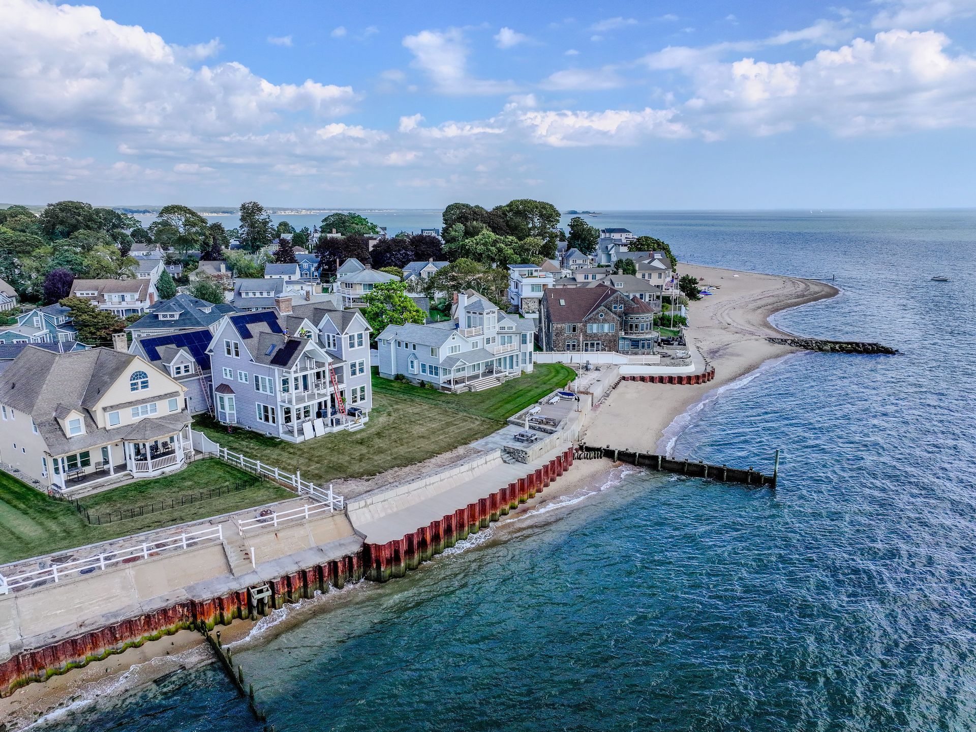 Aerial view of a coastal village with white houses, a red dock, and rocky shoreline beside blue water.