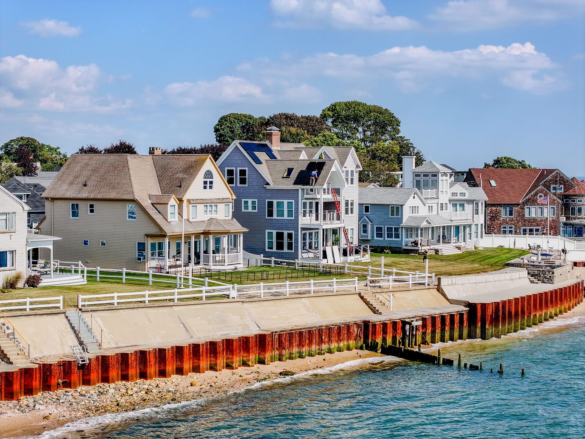 Row of seaside houses along a rocky shore with blue water and a bright sky