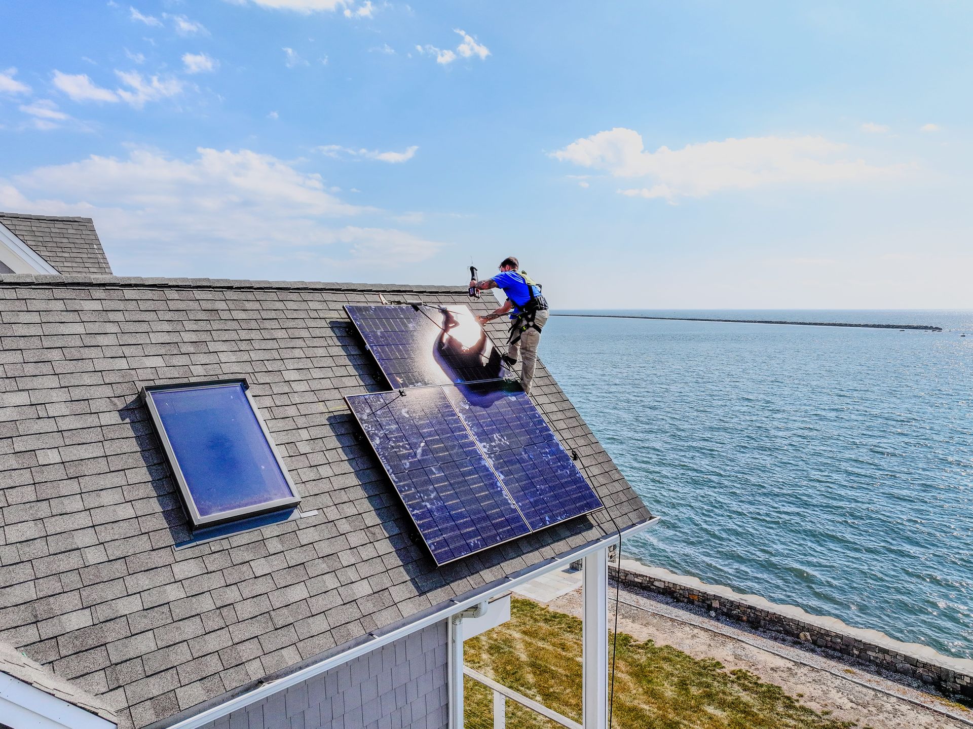 Worker cleaning solar panels on a rooftop beside the ocean